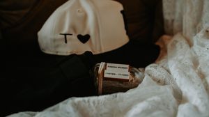 A vintage medicine bottle rests on white fabric next to a white cap with a heart design.