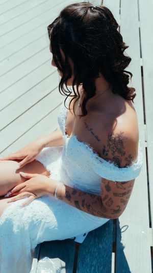 A close-up view of an off-shoulder white lace wedding dress with visible tattoos on the shoulder and back.