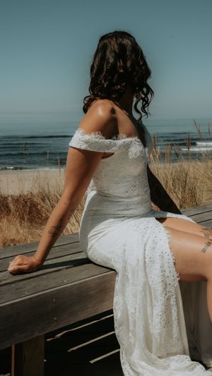 White lace wedding dress details photographed on a wooden boardwalk by the beach.