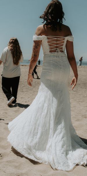 A back view of a corset-style lace wedding dress with a long train on a beach.