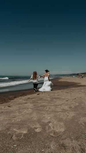 Two people run joyfully along a scenic beach shoreline with waves crashing in the background.