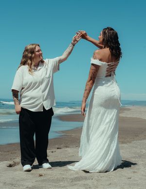 Two people in white and black outfits sitting together on a sandy beach.