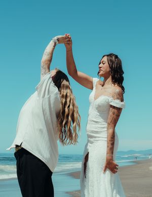 Two people dancing together on a sunny beach with a bright blue sky overhead.