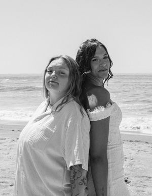 Black and white portrait of two companions embracing on a peaceful beach with waves rolling in.