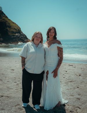 Two people embracing on a scenic beach with cliffs and ocean waves in the background.