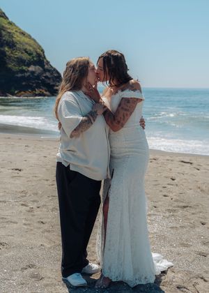A romantic beach wedding ceremony takes place on a sandy shore with cliffs and blue ocean waters in the background.