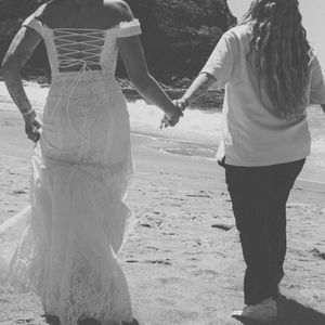 People holding hands and walking together on a beach in black and white wedding attire.