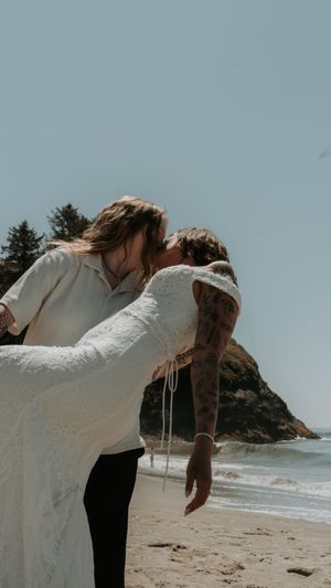 A romantic beach wedding scene with a couple embracing on a sandy shore with a rocky coastline in the background.