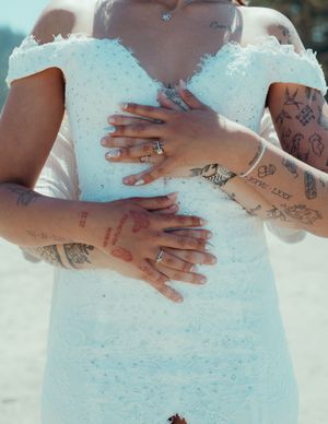 Detail shots of tattooed hands placed lovingly on a textured white wedding gown.