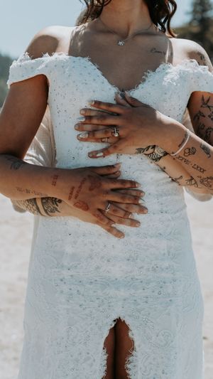 Close-up of tattooed hands against a white lace wedding dress.