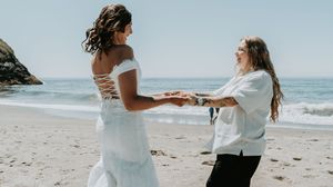 A romantic couple walks and embraces along a scenic beach shoreline on a sunny day.
