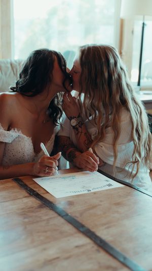 Two people in white dresses sharing an intimate moment while signing documents.