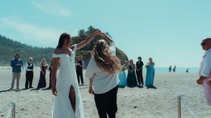 A joyful celebration moment on a beach with onlookers in formal attire watching.