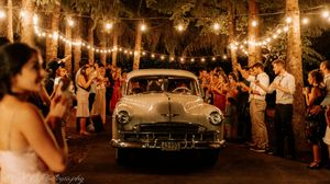 Vintage car illuminated by string lights at nighttime wedding celebration with guests.