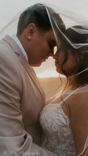 Intimate wedding portrait of couple sharing tender moment under veil at sunset.