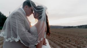 Romantic silhouette of couple embracing in field at sunset with delicate lace veil.