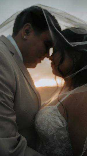 Silhouetted couple sharing an intimate moment under a wedding veil at sunset.