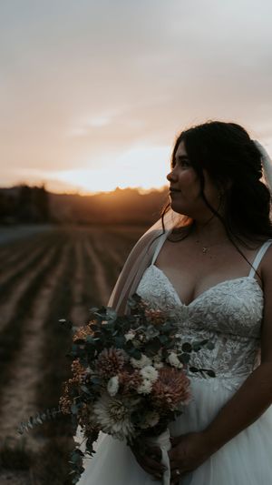 Sunset bridal portrait in a vineyard with moody lighting and autumn-toned bouquet.