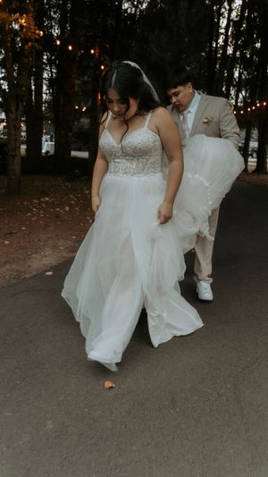 Couple walking together at dusk with the bride's white dress flowing on a garden path.
