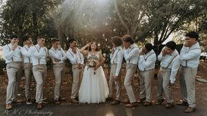 Wedding party poses playfully in casual attire with groomsmen in light colored suits.