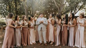 Wedding party members lined up outdoors wearing blush pink and neutral colored dresses for a group photo.