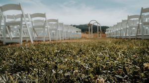 White wedding chairs lined up in rows on a grassy field under a blue sky.
