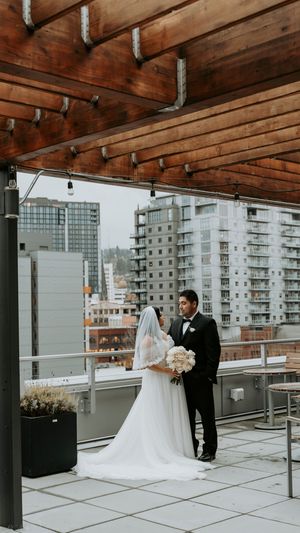 A romantic rooftop wedding moment with city buildings in the background and wooden beams overhead.