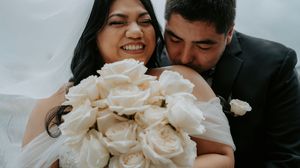 A joyful wedding couple shares an intimate moment with a stunning bouquet of white roses.