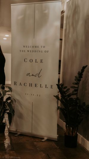 Elegant wedding welcome signs with names Cole and Rachelle displayed on white banners with decorative plants.