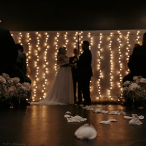 Wedding reception scene with string lights creating a romantic backdrop and dress details on dark floor.
