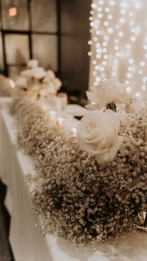 Elegant white roses and baby's breath floral arrangement with twinkling bokeh lights in the background.