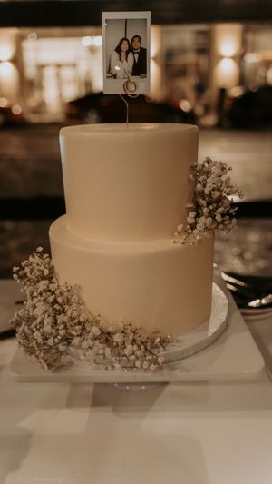 A simple white wedding cake adorned with delicate baby's breath flowers sits elegantly on a white display stand.