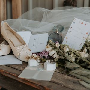 Wedding details including handwritten notes, dried flowers, and candles arranged on a rustic wooden surface.