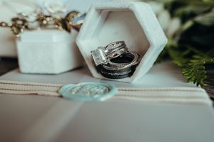 A collection of wedding rings and engagement jewelry displayed on white geometric surfaces with greenery accents.