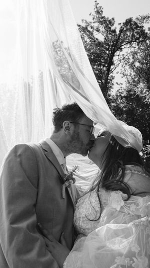 A romantic black and white sequence of a couple kissing behind flowing white veils in an outdoor garden setting.