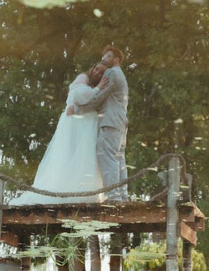 A couple in wedding attire shares an intimate moment on a rustic wooden dock at sunset.