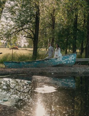 A tranquil pond reflects trees and sunlight with a weathered blue boat resting on its shore.