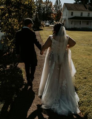 A couple walks hand in hand on a sunny day, with the bride's white wedding dress flowing behind them.