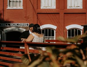 A rustic red brick mill building exterior with white-trimmed windows and industrial architectural details.