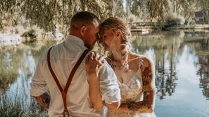 Romantic couple embraces by tranquil lake during sunset photo session in natural outdoor setting.