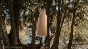 Wedding dresses hang from trees in an enchanting outdoor forest setting creating a dreamy bridal display.