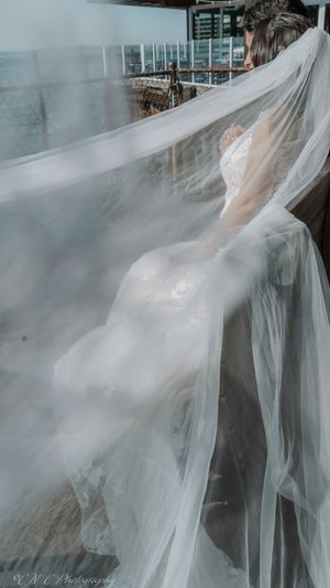 A flowing white wedding veil billows dramatically in the breeze against a dark background.