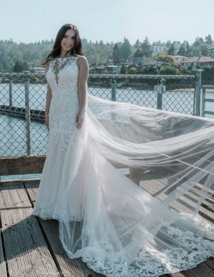 A flowing white wedding dress with lace details billows in the wind on a waterfront deck.