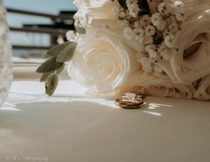 Gold wedding rings resting on a white surface surrounded by delicate white floral arrangements and greenery.