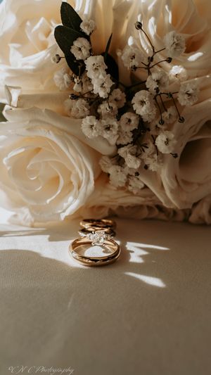 Wedding rings displayed elegantly against white roses and baby's breath flowers in soft lighting.