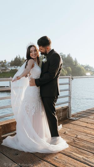 Romantic wedding couple embracing on a wooden pier by the water in bright daylight.