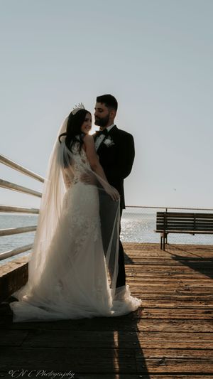 A couple in wedding attire shares an intimate moment on a wooden pier during sunset.