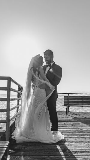 A romantic black and white wedding photo captured on a wooden pier at sunset.