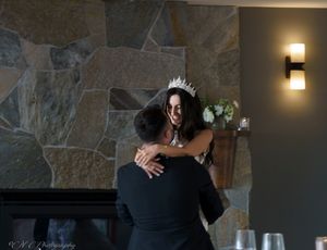 A couple embraces during a wedding celebration in front of a stone wall with ambient lighting.