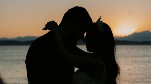 A silhouetted couple embraces against a sunset sky over calm waters.